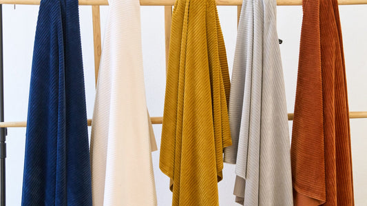 Five removable sofa covers in navy, cream, mustard, grey and terracotta hanging on a garment rail after washing